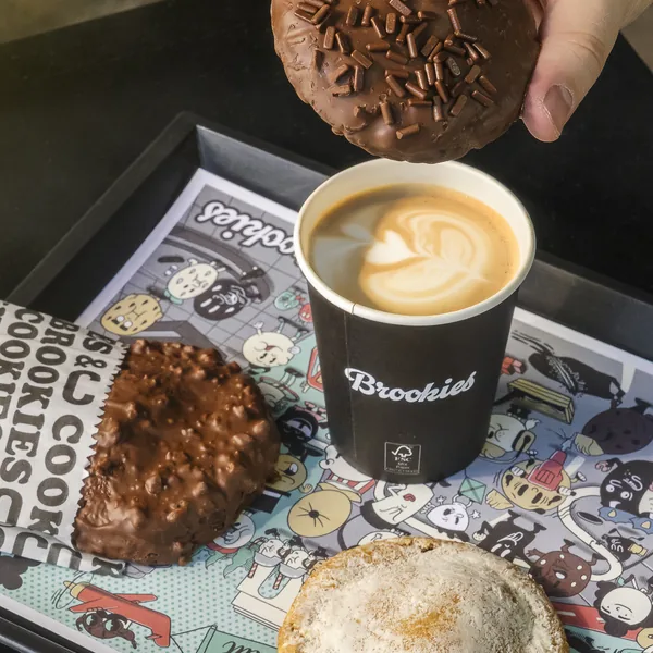 Café com desenho na espuma ao lado de cookies, na bandeja da Brookies